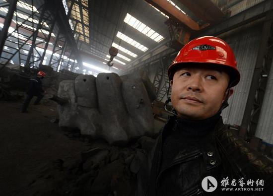 河北唐山一个不锈钢铸造厂，中国艺术家刘勃麟站在他的作品”拳头“雕塑前